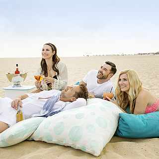 Zwei Pärchen sitzen zusammen am Strand auf Sitzkissen und trinken leckere Drinks