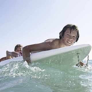 Junge liegt auf einem Surfbrett im Wasser