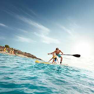 Ein Vater steht mit seinem Sohn gemeinsam auf einem Stand-Up-Paddle-Board
