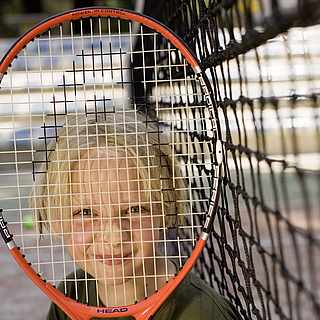 Ein Junge lächelt und hält sich einen Tennisschläger vor das Gesicht