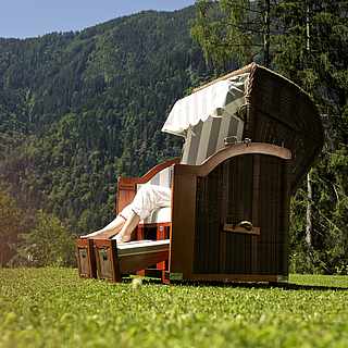 Frau im Strandkorb auf einer Wiese,bewaldeter Berg im Hintegrund