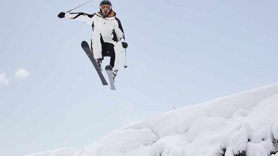 Ein Skifahrer Der gerade über einen kleine Abhang fliegt 