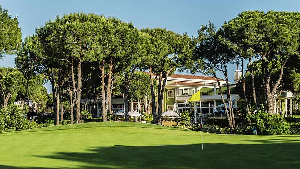 Golfplatz mit Bäumen und Hotel im Hintergrund 