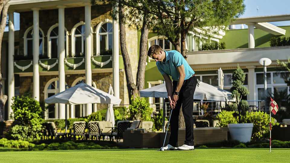 Mann der Golf spielt vor einer Terrasse mit Sitzmöglichkeiten 