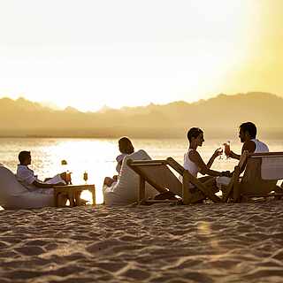 Gäste mit Getränken beim Sonnenuntergang am Strand