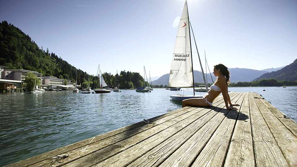 Langer Holzsteg,Frau im Bikini,großes Segelboot im Hintergrund auf den Ossiacher See