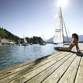 Langer Holzsteg,Frau im Bikini,großes Segelboot im Hintergrund auf den Ossiacher See
