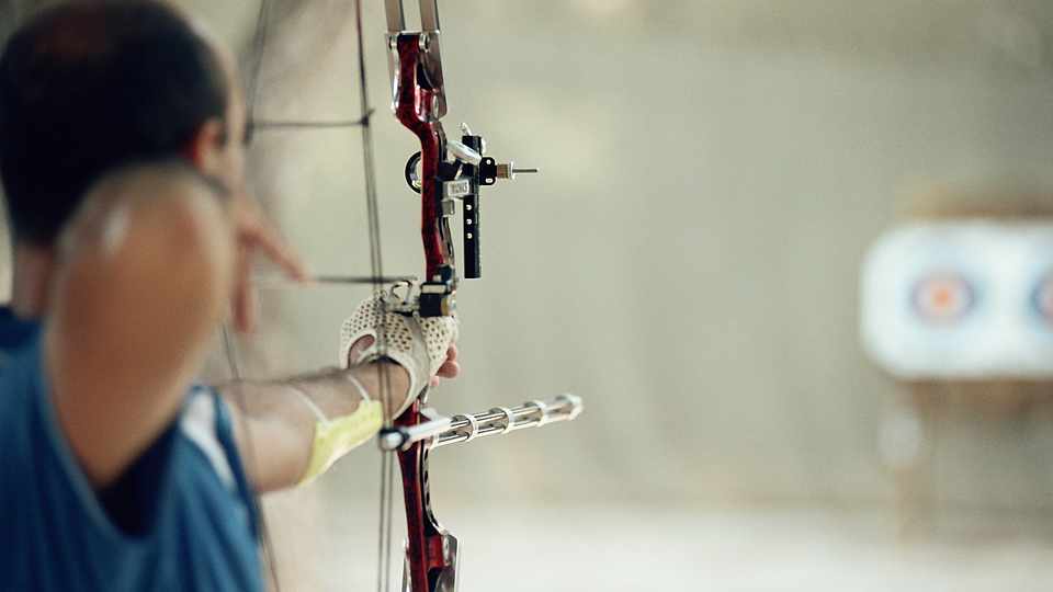 Ein Mann visiert mit einem Bogen ein Ziel an.