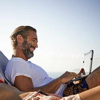 Mann mit Tablet auf Liege.