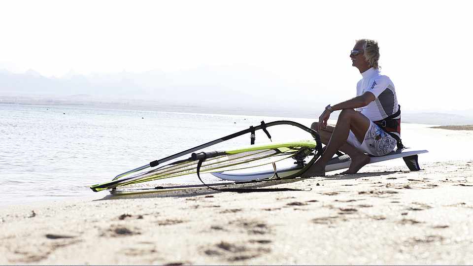 Surfer sitzt auf seinem Surfbrett am Strand und schaut aufs Meer