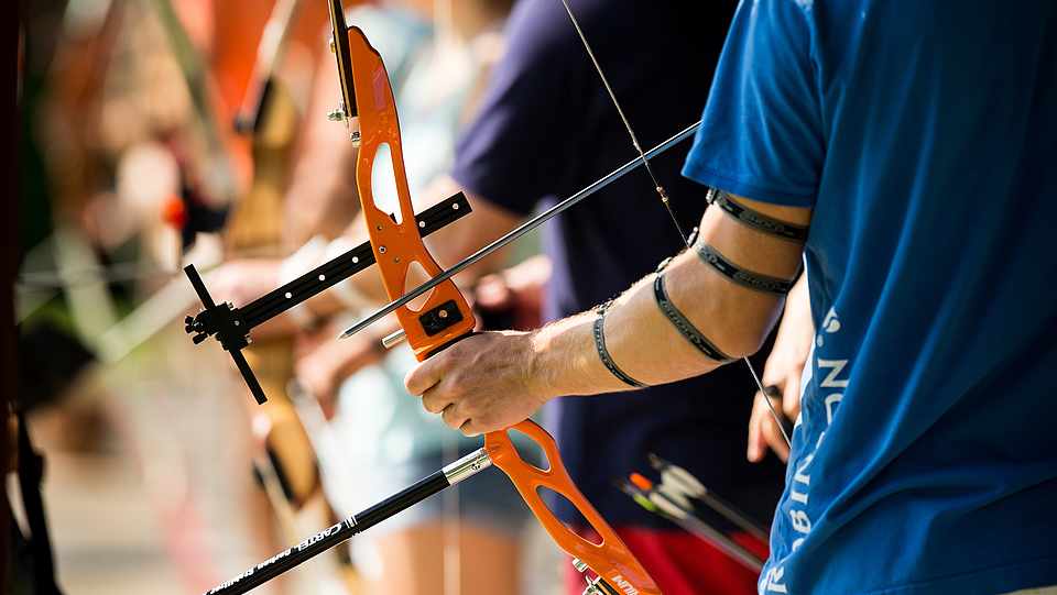 Ein Mann hält einen Bogen. Neben ihm stehen viele anderen mit Pfeil und Bogen.