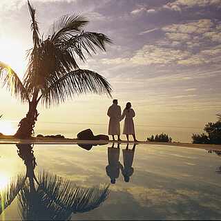 Paar steht im Sonnenuntergang am Pool mit Palmen