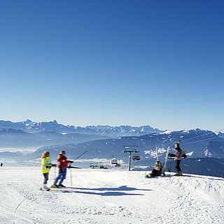 Vier Skifahrer vor einem Gebirge neben einer Seilbahn