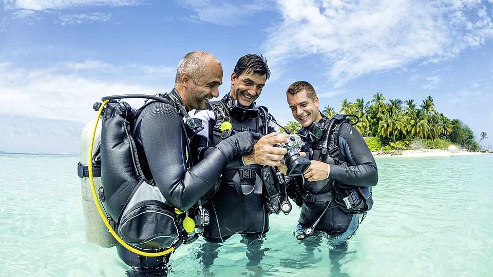 Drei Taucher vorm Tauchgang vor einer Insel