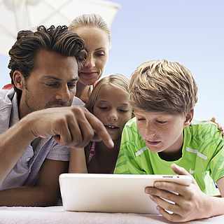 Eine vierköpfige Familie sitzt um das Tablet herum und schaut sich gespannt die ROBINSON App an. 