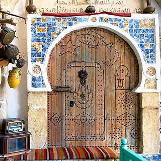 Orientalisch verzierte Holztür mit Rundbogen und bunten Tonkrügen an der Wand